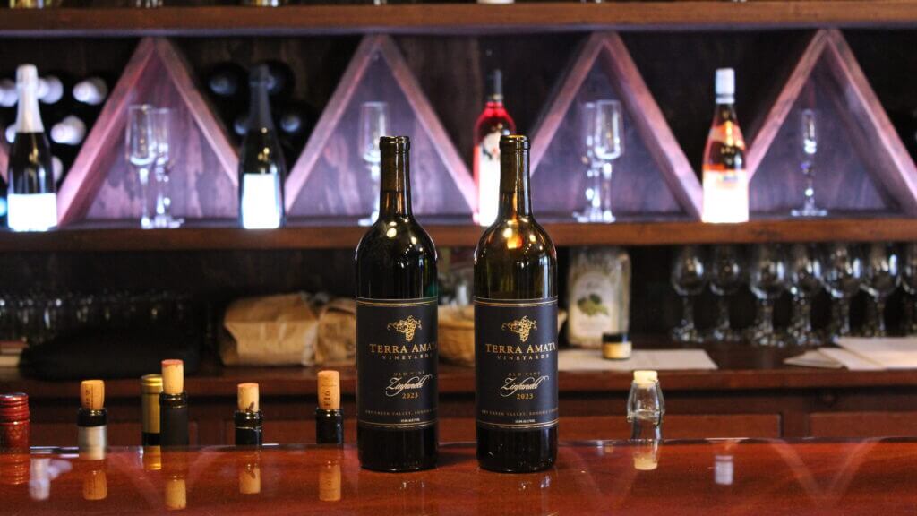 two bottles of zinfandel sitting on a counter that is illuminated from behind, highlighting a pop of purple