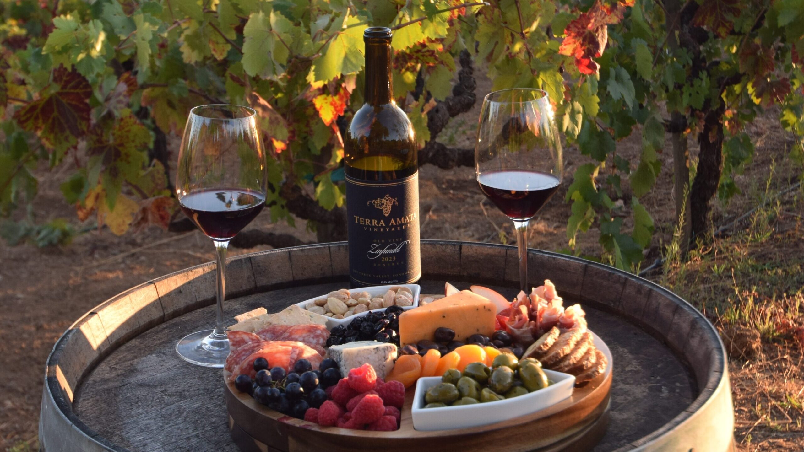 wine barrel with a charcuterie board and two glasses of Zinfandel sitting on top of it